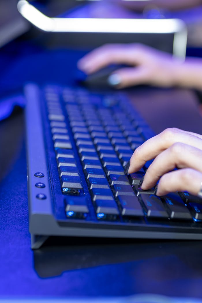 Close-up view of hands typing on a computer keyboard with a blue ambient light.